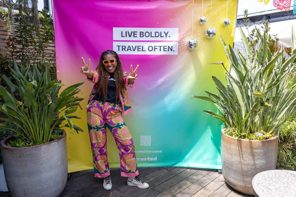 Trusted Community leader, Britt, posing in front of a banner that reads "Live Boldly. Travel Often."at a Trusted event in California!