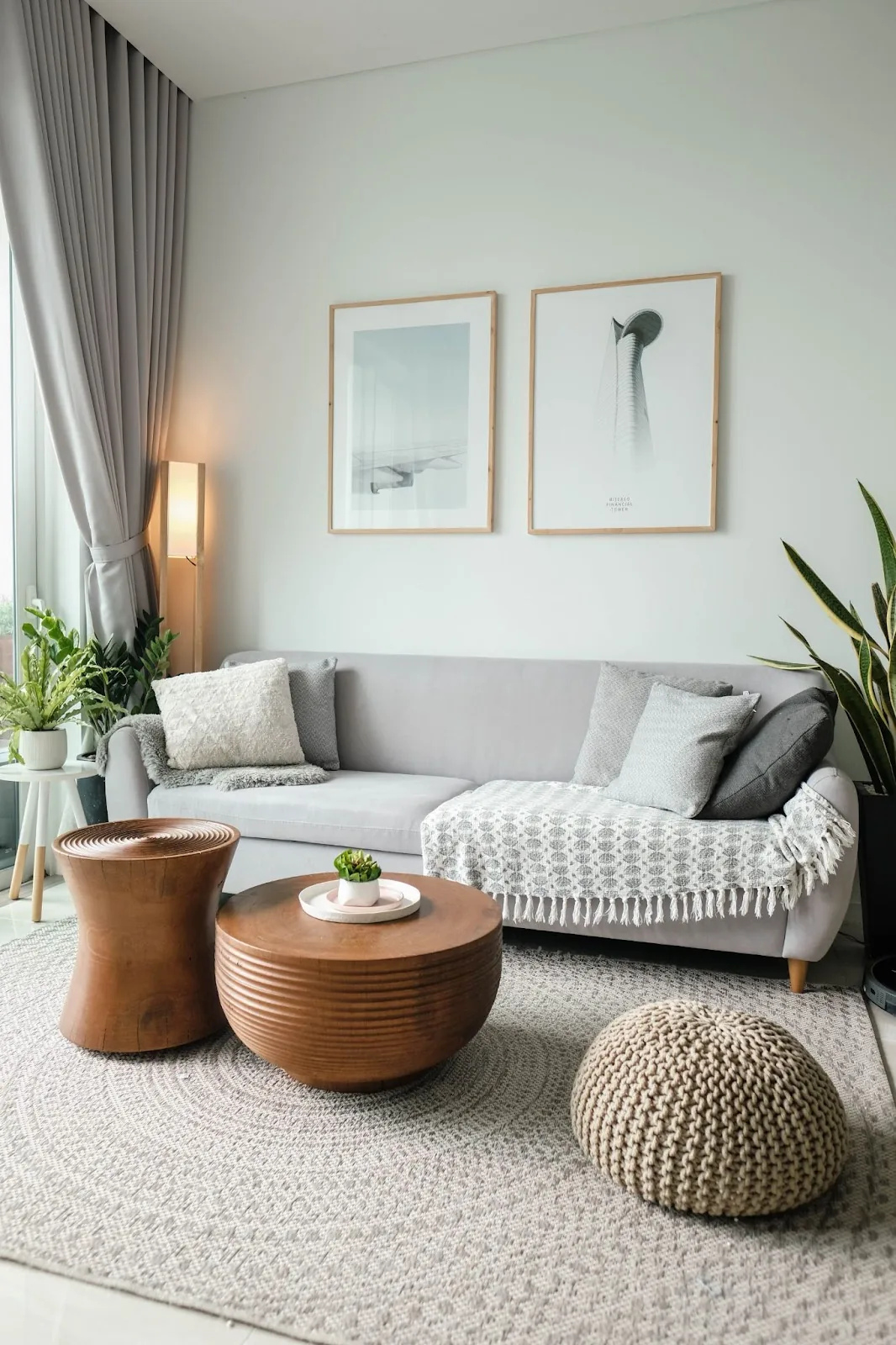 A modern living room setup featuring a neutral-toned sofa adorned with comfortable cushions, complemented by a wooden round coffee table and cozy knit pouf, creating an inviting space for visitors.