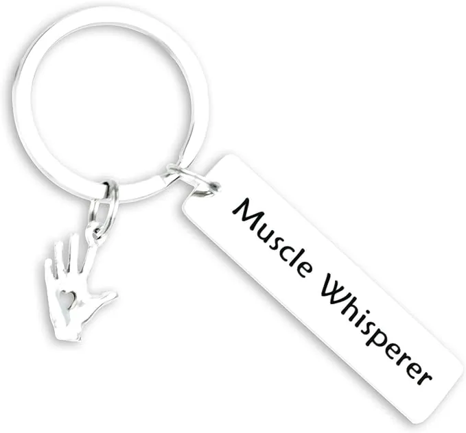A shiny silver keychain featuring a rectangular pendant with 'Muscle Whisperer' engraved in black, alongside a charm of a hand making a love sign. This elegant and affirming accessory is a perfect nod to a physical therapist's skillful touch