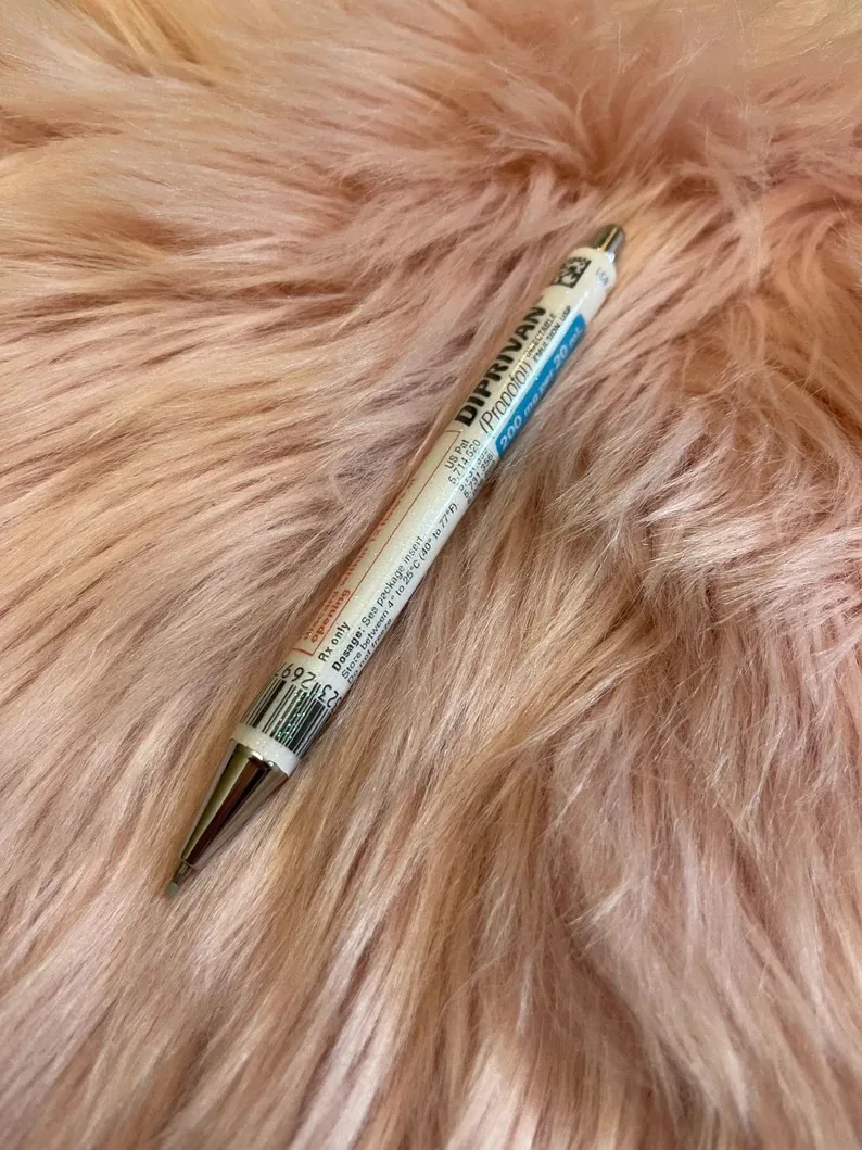 A pen designed to resemble a propofol (Diprivan) vial resting on a plush pink surface, a creative and refillable writing instrument for surgical technicians.